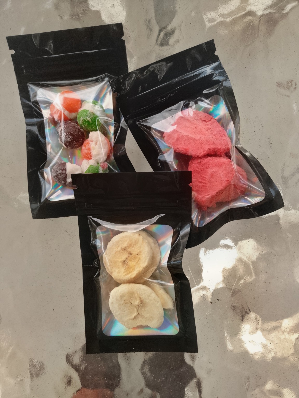 Three holographic black pouches of freeze-dried Halloween candy, strawberries, and bananas